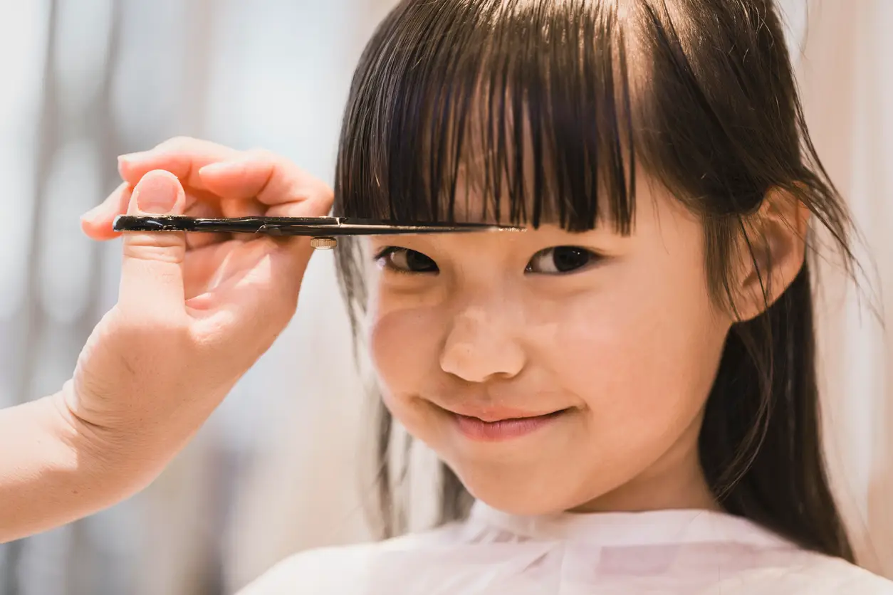 Asian girl having her forelock cut by beautician.
